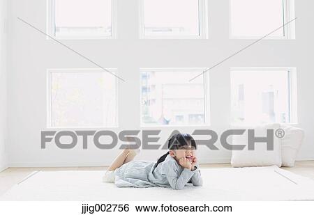 Stock Photograph - Elementary age girl laying on the floor by the window. Fotosearch
