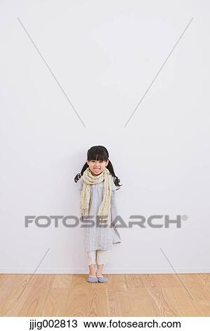 Stock Image - Elementary age girl leaning against a white wall and smiling at camera. Fotosearch
