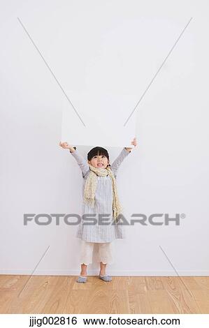 Stock Photograph - Elementary age girl leaning against a white wall and smiling at camera. Fotosearch