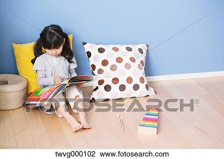 Stock Image - Elementary age girl reading an illustrated book on the floor of the kids room. Fotosearch