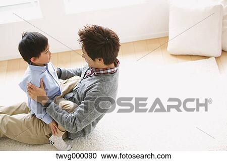 Stock Image - Father laying on the floor and playing with his son while laughing. Fotosearch