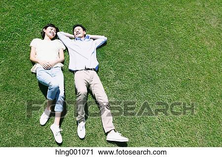 Stock Image - Happy Japanese couple laying on grass in a park. Fotosearch