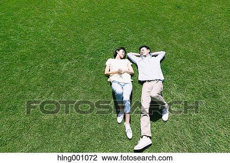 Stock Image - Happy Japanese couple laying on grass in a park. Fotosearch