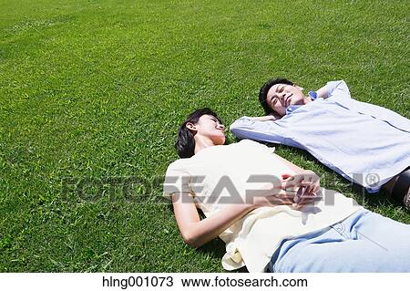 Stock Image - Happy Japanese couple laying on grass in a park. Fotosearch