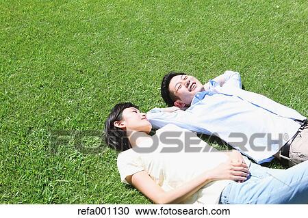 Stock Image - Happy Japanese couple laying on grass in a park. Fotosearch