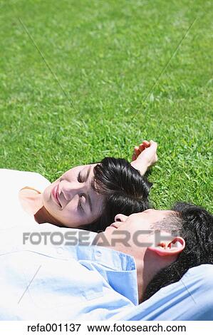 Stock Photo - Happy Japanese couple laying on grass in a park. Fotosearch