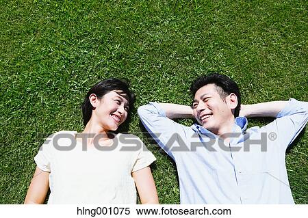 Stock Photography - Happy Japanese couple laying on grass in a park. Fotosearch