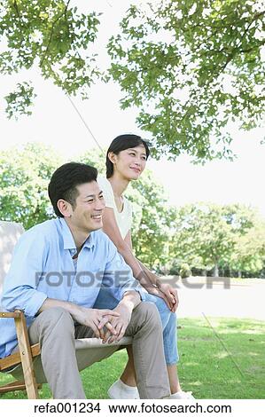 Picture - Happy Japanese couple with deck chair in a park. Fotosearch