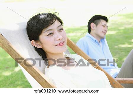 Stock Image - Happy Japanese couple with deck chair in a park. Fotosearch