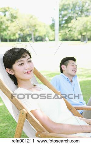 Stock Image - Happy Japanese couple with deck chair in a park. Fotosearch