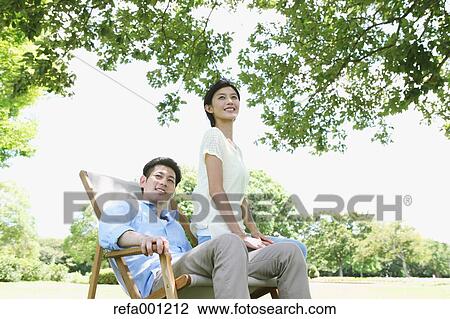 Stock Image - Happy Japanese couple with deck chair in a park. Fotosearch