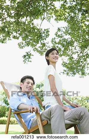 Stock Image - Happy Japanese couple with deck chair in a park. Fotosearch