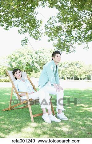 Stock Photo - Happy Japanese couple with deck chair in a park. Fotosearch