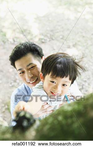 Stock Image - Happy Japanese father and son catching insects in a city park. Fotosearch