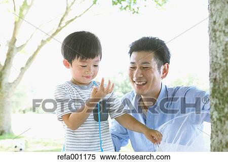 Stock Photography - Happy Japanese father and son catching insects in a city park. Fotosearch