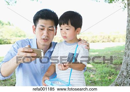Stock Photography - Happy Japanese father and son catching insects in a city park. Fotosearch