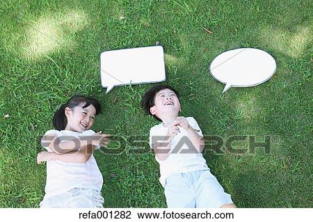 Stock Image - Happy Japanese kids laying with whiteboards in a city park. Fotosearch