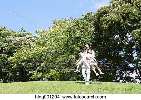 Picture - Japanese father playing with his kids in a city park. Fotosearch
