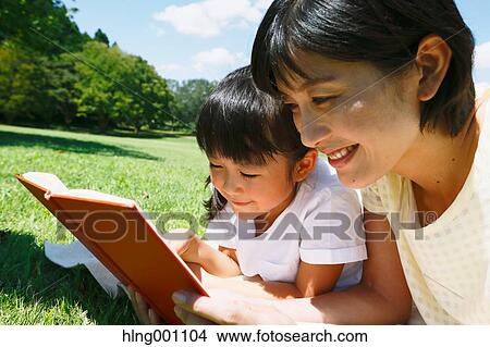 Picture - Japanese mother and daughter reading a book in a city park. Fotosearch