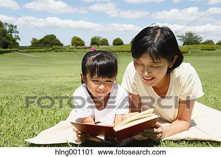 Stock Image - Japanese mother and daughter reading a book in a city park. Fotosearch
