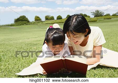 Stock Image - Japanese mother and daughter reading a book in a city park. Fotosearch