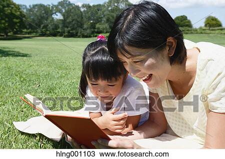 Stock Image - Japanese mother and daughter reading a book in a city park. Fotosearch