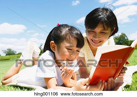 Stock Photograph - Japanese mother and daughter reading a book in a city park. Fotosearch