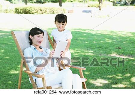 Japanese mother and daughter with tablet in a city park View Large Photo Image Picture - Japanese mother and daughter with tablet in a city park. Fotosearch