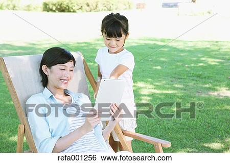 Stock Photograph - Japanese mother and daughter with tablet in a city park. Fotosearch