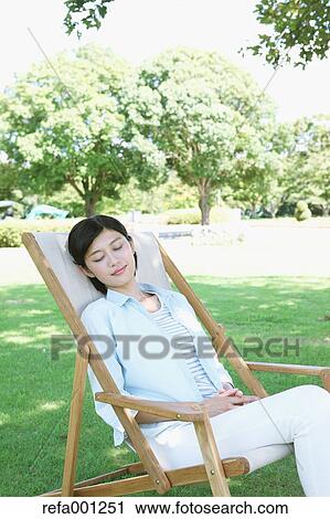 Stock Image - Japanese woman resting on deck chair in a city park. Fotosearch