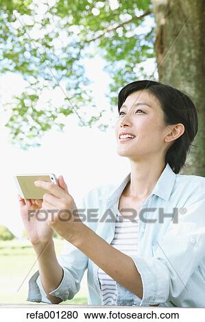 Japanese woman with smartphone in a city park View Large Photo Image Stock Image - Japanese woman with smartphone in a city park. Fotosearch