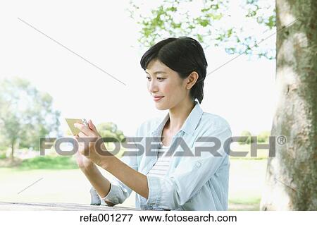 Stock Photo - Japanese woman with smartphone in a city park. Fotosearch