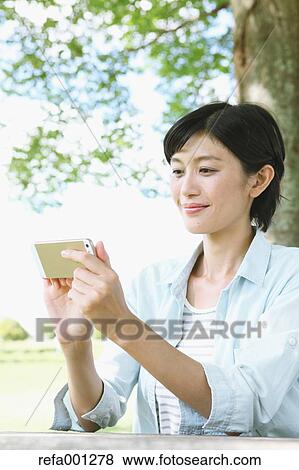 Japanese woman with smartphone in a city park View Large Photo Image Stock Photo - Japanese woman with smartphone in a city park. Fotosearch