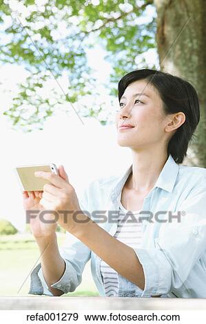 Stock Photo - Japanese woman with smartphone in a city park. Fotosearch
