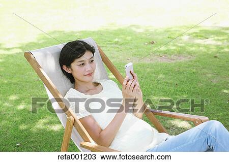 Japanese woman with smartphone on deck chair in a city park View Large Photo Image Stock Image - Japanese woman with smartphone on deck chair in a city park. Fotosearch