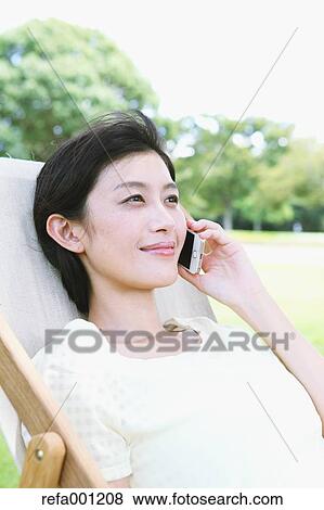 Japanese woman with smartphone on deck chair in a city park View Large Photo Image Stock Photo - Japanese woman with smartphone on deck chair in a city park. Fotosearch