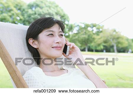 Japanese woman with smartphone on deck chair in a city park View Large Photo Image Stock Photo - Japanese woman with smartphone on deck chair in a city park. Fotosearch