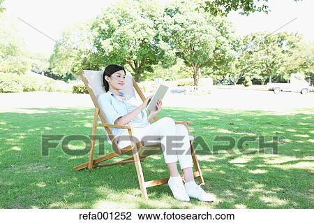 Japanese woman with tablet on deck chair in a city park View Large Photo Image Stock Image - Japanese woman with tablet on deck chair in a city park. Fotosearch