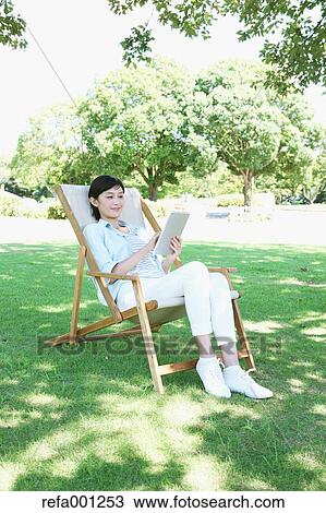 Japanese woman with tablet on deck chair in a city park View Large Photo Image Stock Image - Japanese woman with tablet on deck chair in a city park. Fotosearch