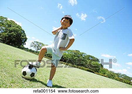 Picture - Japanese young boy playing soccer in a city park. Fotosearch
