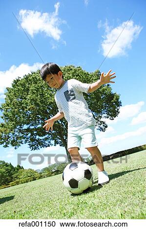 Stock Image - Japanese young boy playing soccer in a city park. Fotosearch