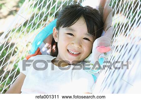 Stock Image - Japanese young girl on hammock in a city park. Fotosearch