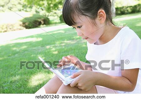 Japanese young girl playing video games in a city park View Large Photo Image Stock Image - Japanese young girl playing video games in a city park. Fotosearch