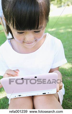 Japanese young girl playing video games in a city park View Large Photo Image Stock Photo - Japanese young girl playing video games in a city park. Fotosearch