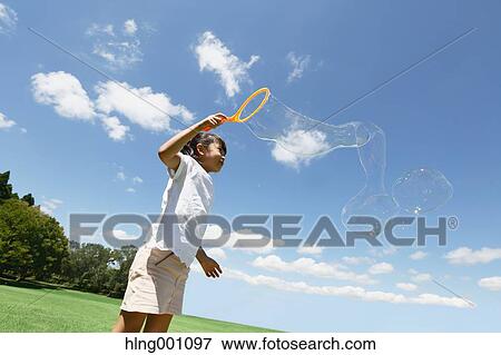 Stock Photo - Japanese young girl playing with soap bubbles in a city park. Fotosearch