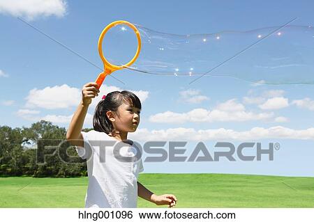 Japanese young girl playing with soap bubbles in a city park View Large Photo Image Stock Photograph - Japanese young girl playing with soap bubbles in a city park. Fotosearch