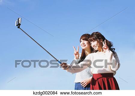 Two young Japanese women taking a selfie with selfie stick View Large Photo Image Picture - Two young Japanese women taking a selfie with selfie stick. Fotosearch