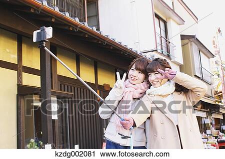 Stock Image - "Two young Japanese women taking a selfie in Kawagoe old town, Japan". Fotosearch