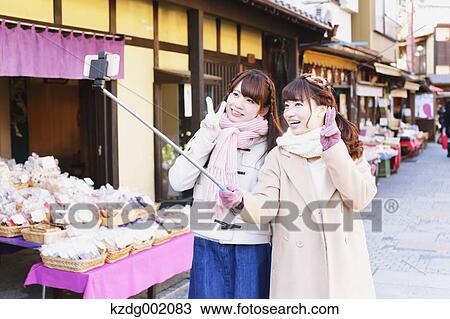 Stock Image - "Two young Japanese women taking a selfie in Kawagoe old town, Japan". Fotosearch