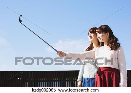 Two young Japanese women taking a selfie with selfie stick View Large Photo Image Stock Photography - Two young Japanese women taking a selfie with selfie stick. Fotosearch